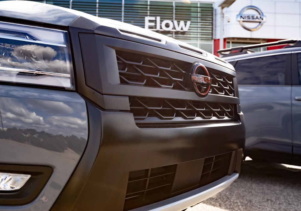 Close up of the front grille of a Nissan vehicle parked outside of the Flow Nissan dealership
